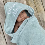 Baby gewikkeld in oudgroene badcape die geborduurd is met naam