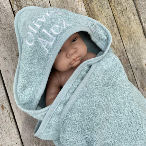 Baby gewikkeld in oudgroene badcape die geborduurd is met naam